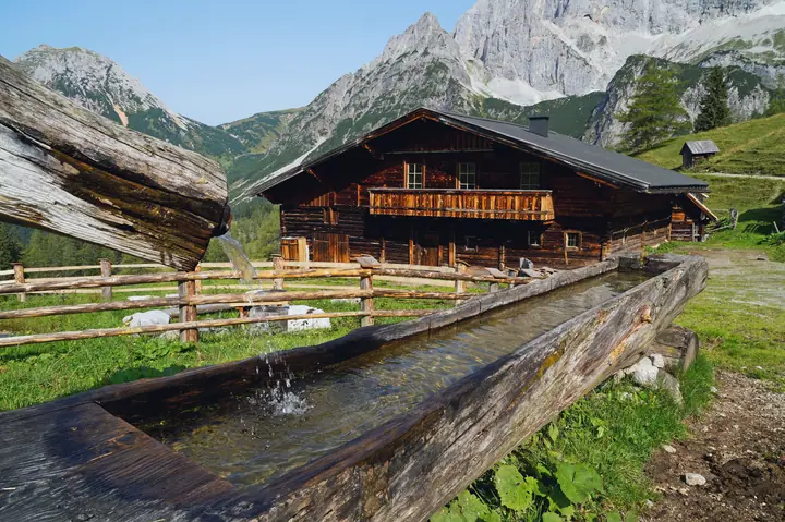 Wooden alpine hut with a fountain in front of rocky mountains