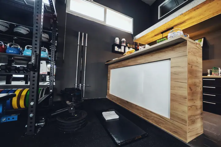 Strength area of a gym: rack with kettlebells and medicine balls, three barbells on the wall, weight plates and a training mat with a towel in front