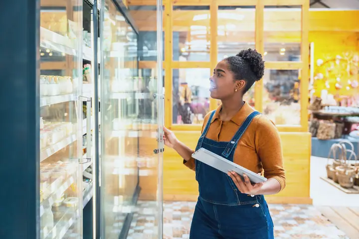 Employee checks a refrigerated shelf, holding a tablet