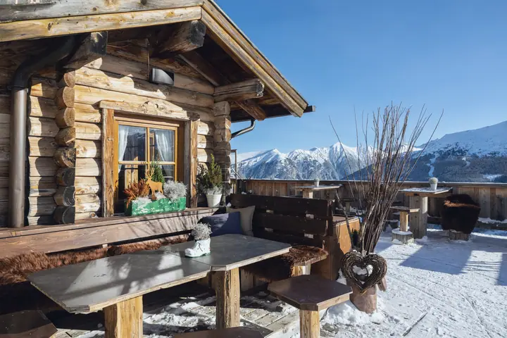 Wooden hut with a terrace in the snow, snowy mountains behind it
