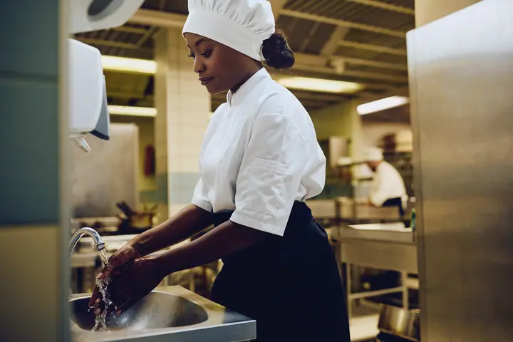 A cook in a cap washes her hands in the professional kitchen