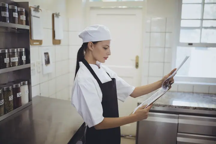 A cook in a cap reads documents in the kitchen