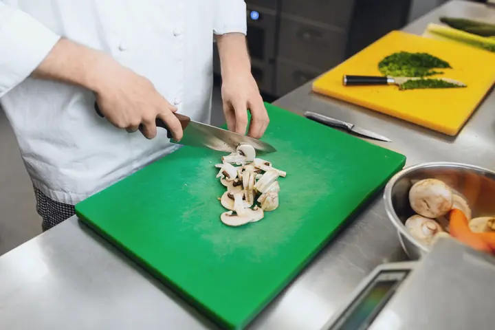 Mushrooms are cut on a green board, a yellow board for herbs behind it