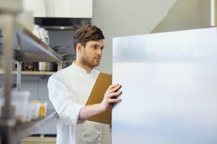 A cook with a clipboard in front of the fridge