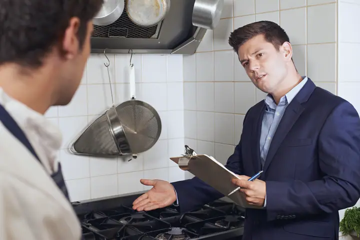 An inspector in a suit with a clipboard at the stove