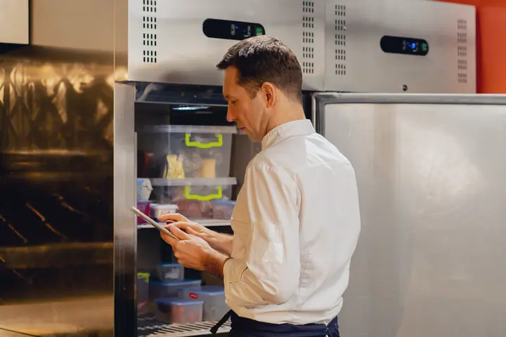 Employee checks the open fridge and taps on a tablet