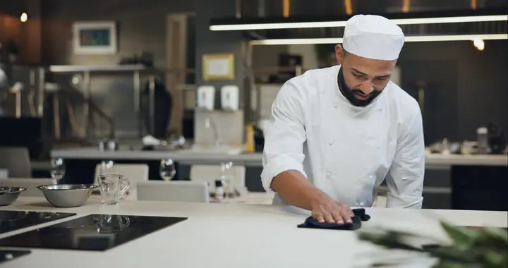 Chef in a cap wipes down the work surface after closing