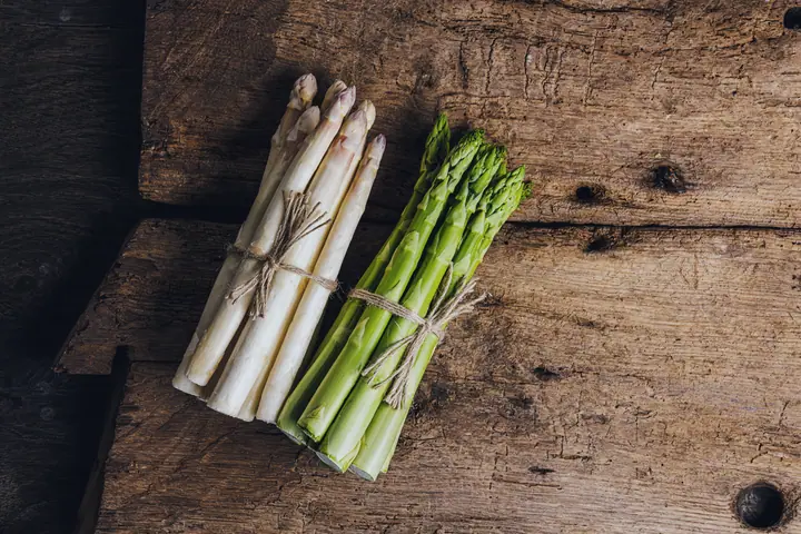 White and green asparagus bundled on dark wood
